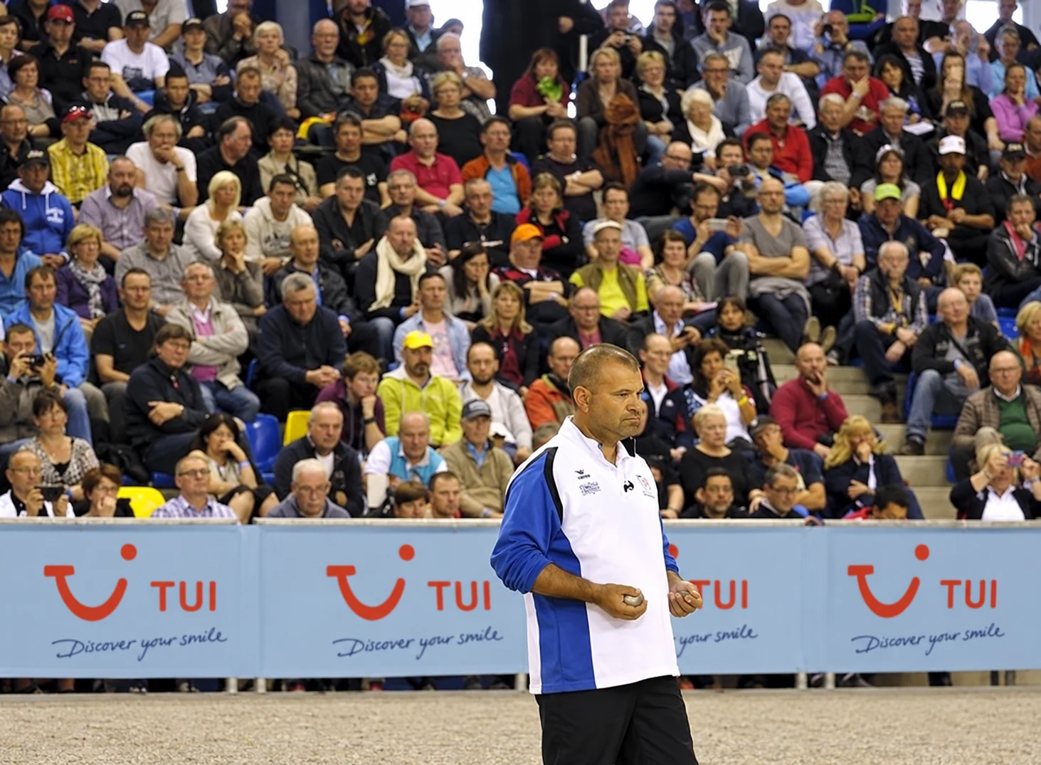 Petanquespeler met boules voor een volle tribune