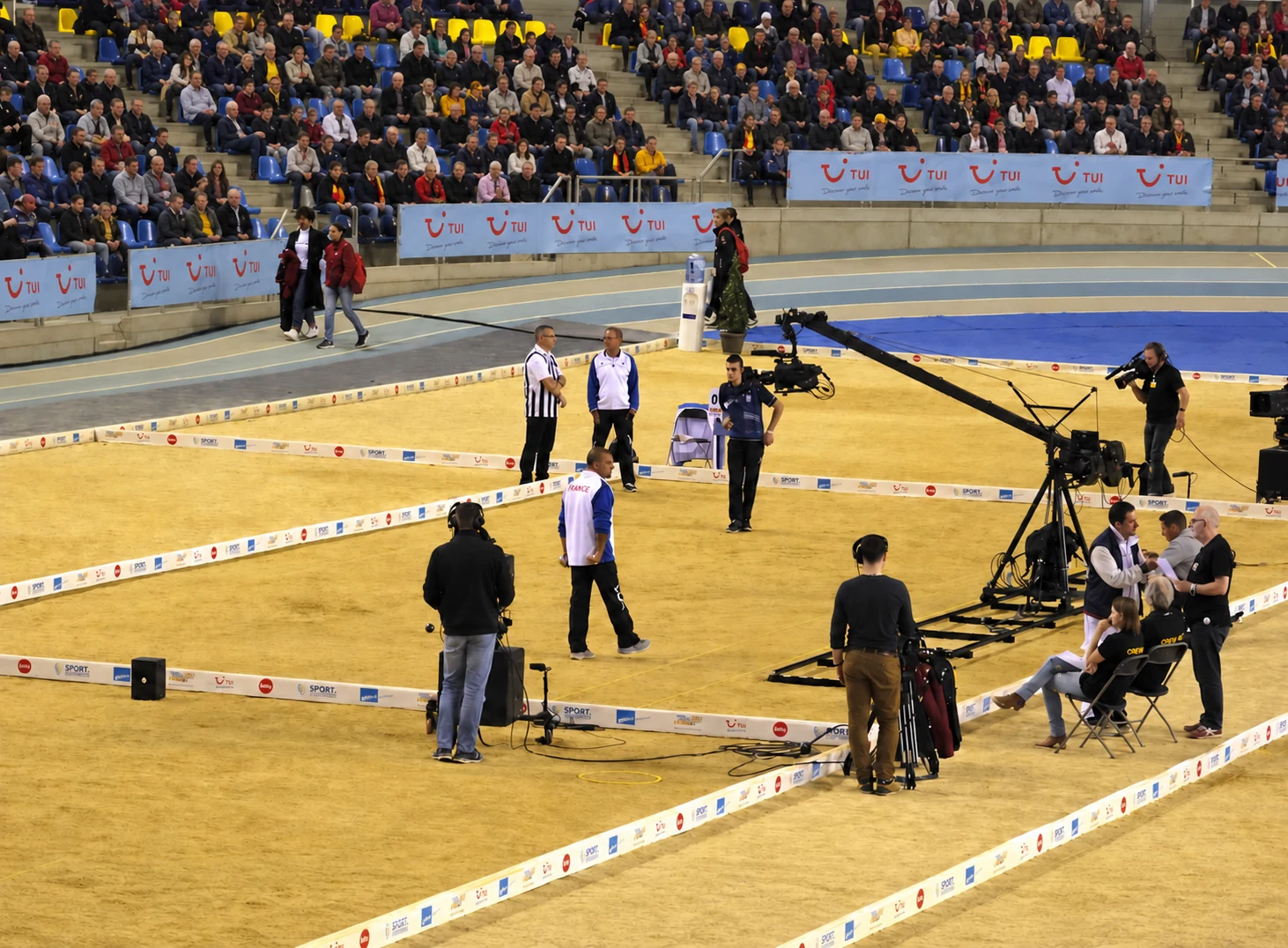 Overzicht van indoor petanqueterreinen, spelers en een camerakraan